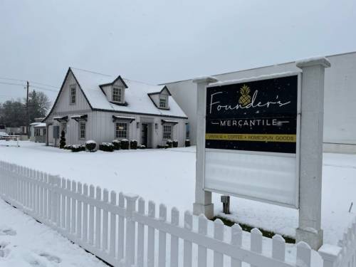 A snow-covered building with a sign reading "Founders Mercantile," featuring vintage items, coffee, and homespun goods.
