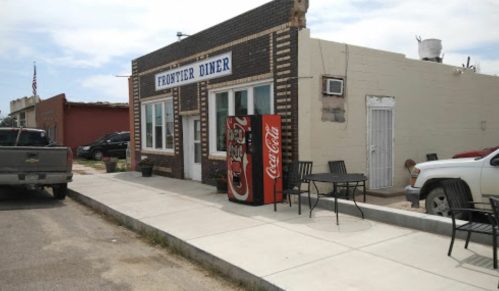 A small diner with a Coca-Cola vending machine outside, featuring a brick facade and outdoor seating.