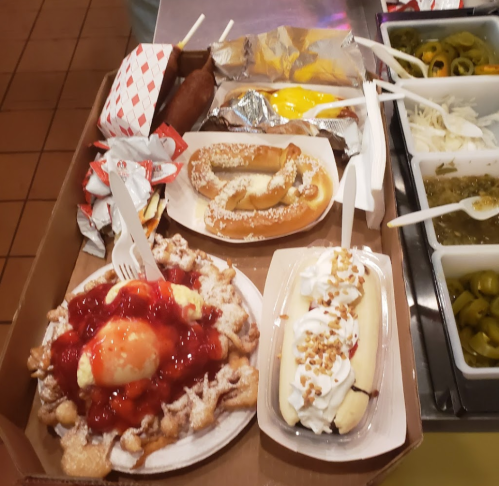 A tray of assorted desserts including funnel cake with strawberries, a banana split, and pretzels.