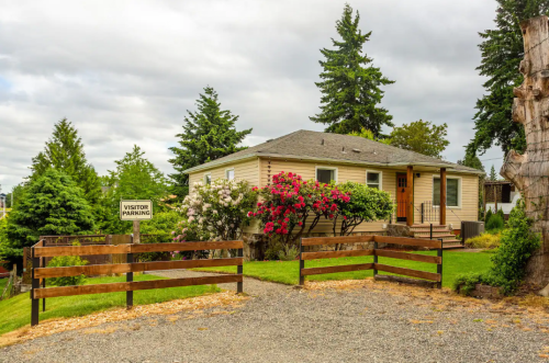A single-story house with a garden, surrounded by trees, and a sign for visitor parking in front.