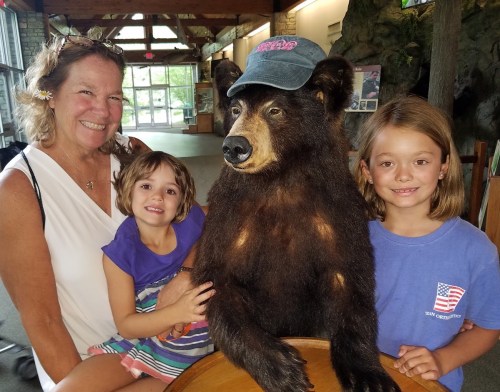A woman and two girls pose with a life-sized bear statue wearing a cap in a museum setting.
