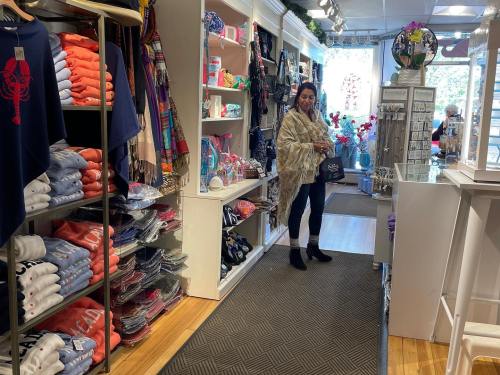 A woman in a shawl stands in a colorful retail store, surrounded by neatly arranged clothing and accessories.