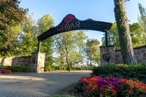 Entrance archway to Gervasi Vineyard, surrounded by trees and colorful flowers.