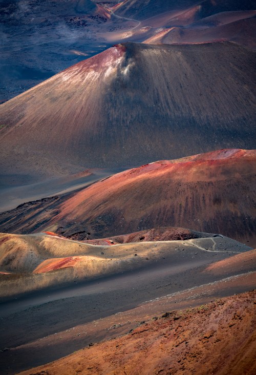 Aerial view of colorful volcanic craters and slopes, showcasing rich earth tones and rugged terrain.