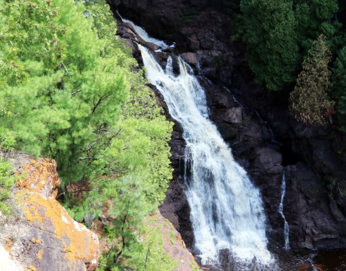 A cascading waterfall flows down rocky terrain, surrounded by lush green trees and vibrant moss.