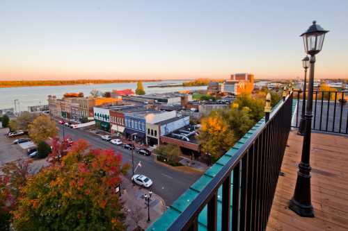 A scenic view of a riverside town at sunset, featuring buildings, trees, and a calm river in the background.