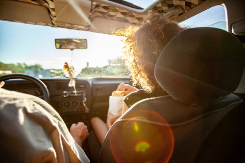 A person in the passenger seat enjoys food while sunlight streams through the car's interior.