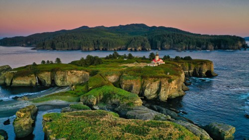 Aerial view of a coastal landscape featuring a lighthouse on a rocky island surrounded by water and lush greenery.