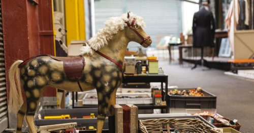 A vintage wooden horse toy stands beside various collectibles in a market setting.