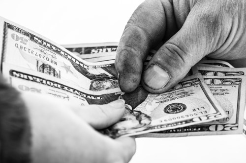 Two hands exchanging crumpled twenty-dollar bills in black and white.