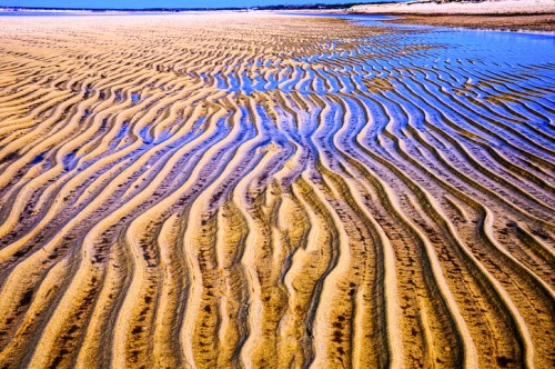Rippling sand patterns and shallow water create a textured landscape on a beach at low tide.