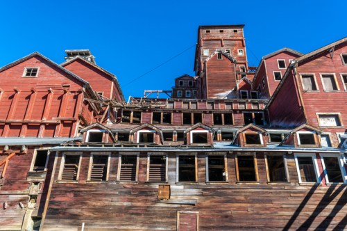 Abandoned red wooden buildings with multiple levels against a clear blue sky.