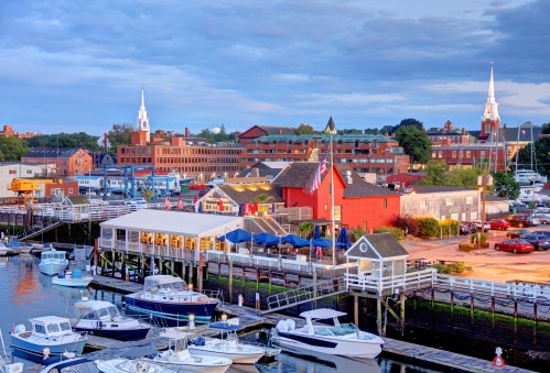 A scenic waterfront view featuring boats, a marina, and charming buildings under a cloudy sky.