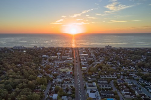 Aerial view of a coastal town at sunset, with the sun reflecting on the water and trees lining the streets.