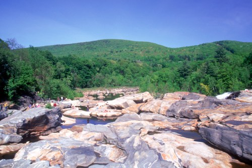 A scenic view of rocky terrain and lush green hills under a clear blue sky, with people enjoying the natural landscape.