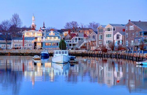 A serene harbor at dusk, featuring colorful houses and boats reflecting in calm water.