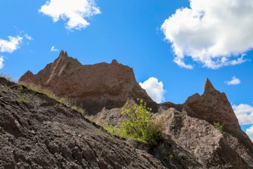 Rocky peaks rise against a bright blue sky with fluffy clouds, surrounded by sparse vegetation.