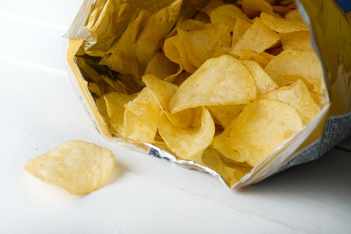 A partially open bag of potato chips with a few chips spilling out onto a white surface.