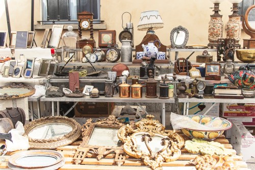 A bustling antique market stall filled with clocks, frames, lamps, and various vintage items on display.