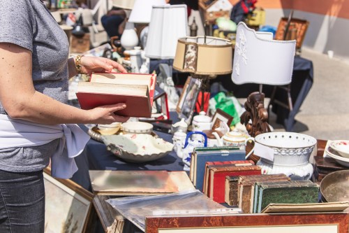 A person holds a red book while browsing a table filled with various antiques and collectibles.