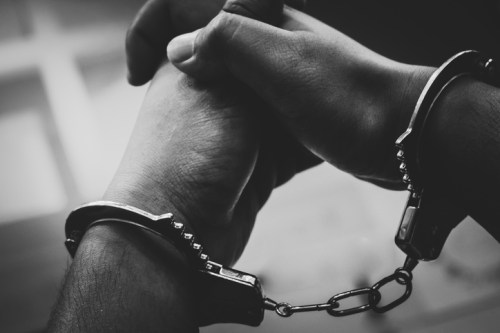 Two hands are clasped together, connected by silver handcuffs, in a black and white image.