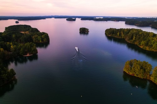 Aerial view of a serene lake with islands and a boat creating ripples in the water during sunset.