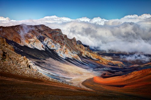 A stunning landscape of colorful volcanic mountains under a blue sky with clouds, showcasing diverse geological formations.