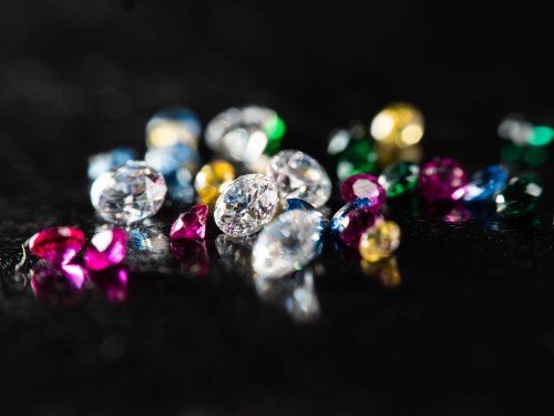 A collection of colorful gemstones scattered on a dark surface, reflecting light in various hues.