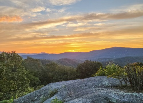 A vibrant sunset over rolling hills, with a rocky foreground and colorful clouds in the sky.