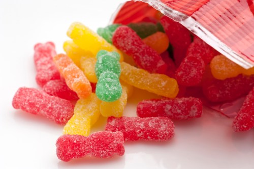 Colorful gummy candies in red, green, and yellow spilling from an open bag onto a white surface.