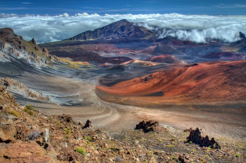 A colorful volcanic landscape with rugged terrain, clouds hovering over the mountains in the background.