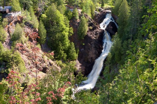 A cascading waterfall flows through rocky terrain, surrounded by lush green trees and vibrant foliage.