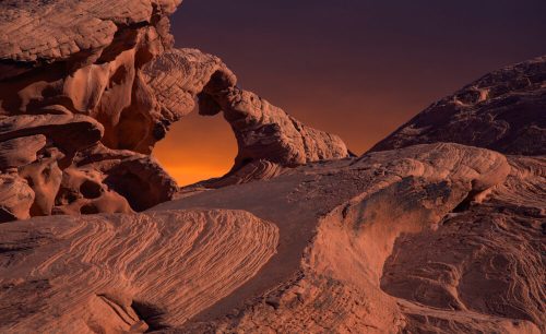A stunning rock formation with an arch, set against a vibrant sunset sky in a desert landscape.