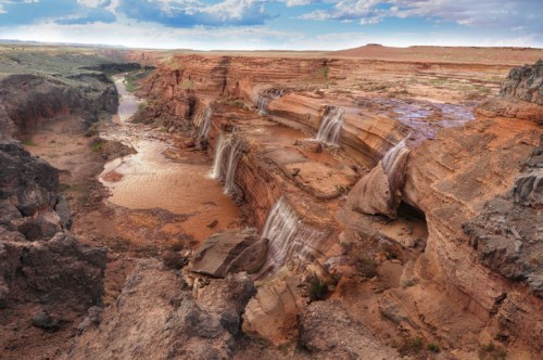 A stunning landscape featuring cascading waterfalls over rocky cliffs, surrounded by a winding river and blue sky.