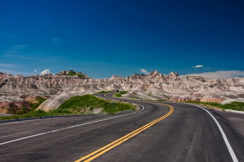 A winding road curves through a rugged landscape of layered rock formations under a clear blue sky.