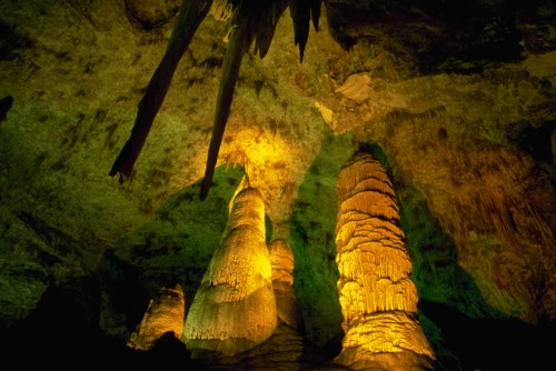 Stalactites and stalagmites illuminated in a colorful cave, showcasing unique rock formations and textures.
