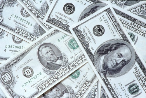 A close-up of various U.S. banknotes, including $50 and $100 bills, scattered on a surface.