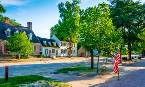 A scenic street lined with trees and historic buildings, featuring an American flag in the foreground.
