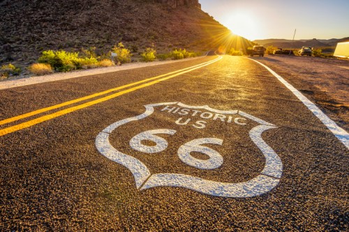 A winding road with a "Historic US 66" sign, bathed in golden sunlight at sunset.