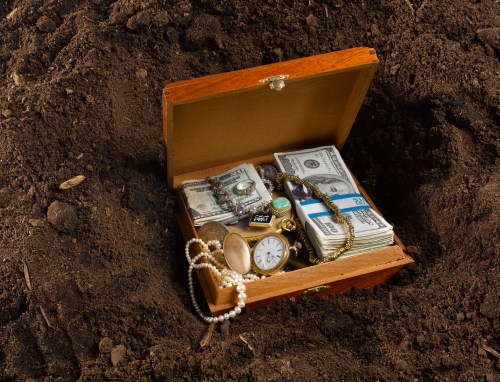 A wooden treasure chest filled with cash, jewelry, and a pocket watch, partially buried in dark soil.