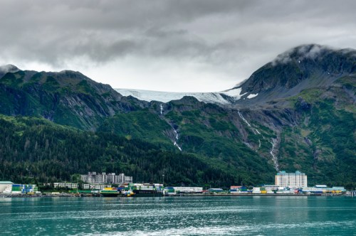 A scenic view of mountains with a glacier, surrounded by lush greenery and a harbor with colorful buildings.