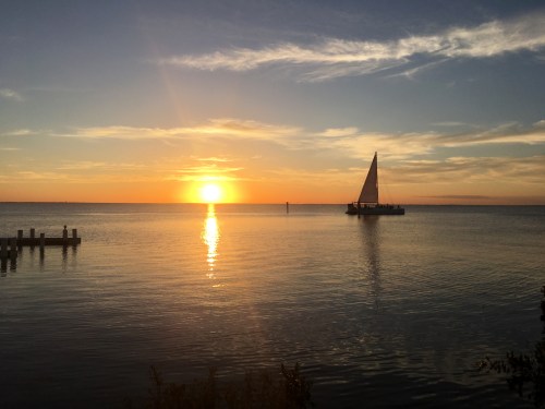 A serene sunset over calm waters, with a sailboat silhouetted against the vibrant sky.
