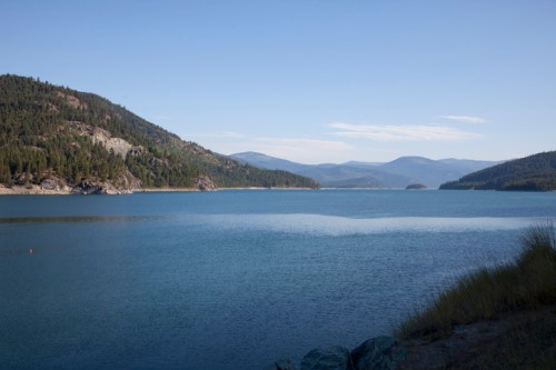A serene lake surrounded by mountains under a clear blue sky, with gentle ripples on the water's surface.