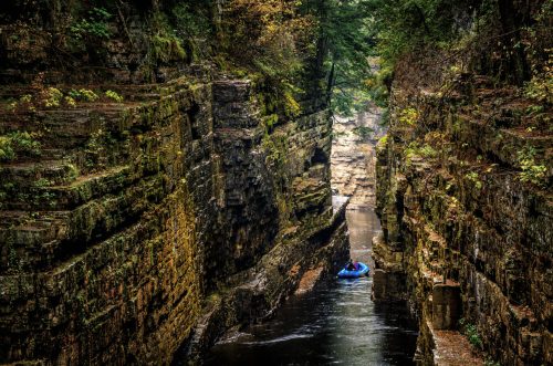 A narrow canyon with steep, moss-covered walls and a small boat navigating the calm waters below.