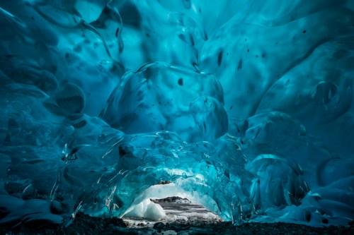 A stunning ice cave with vibrant blue hues and intricate ice formations, illuminated from an opening in the distance.