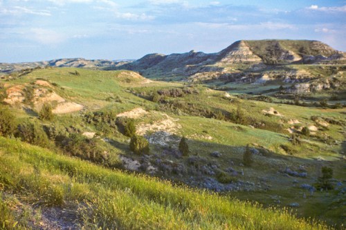 A scenic view of rolling green hills and rugged terrain under a blue sky with scattered clouds.