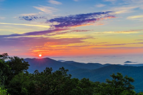 A vibrant sunset over rolling mountains, with colorful clouds and a misty valley below.