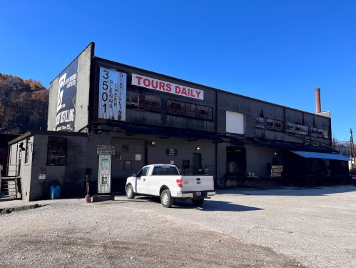 A gray building with a sign for daily tours, parked white truck, and clear blue sky in the background.