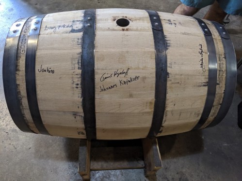 A wooden barrel with metal bands, featuring signatures and names written on its surface.