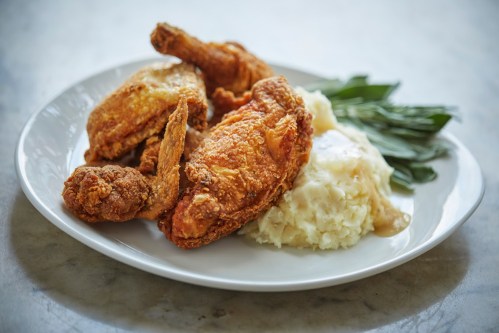 A plate of crispy fried chicken with mashed potatoes and green beans on a light background.
